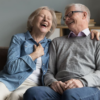 Elderly couple laughing together while sitting on a couch